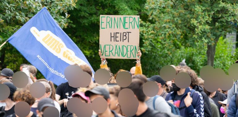 Aus der Menschenmenge der Demonstration hält eine Person ein Schild mit der Aufschrift "Erinnern heißt Verändern" hoch